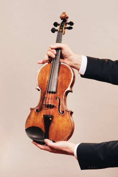 A close up of a classic violin held carefully by hands against a plain background, 2K Phone Wallpaper