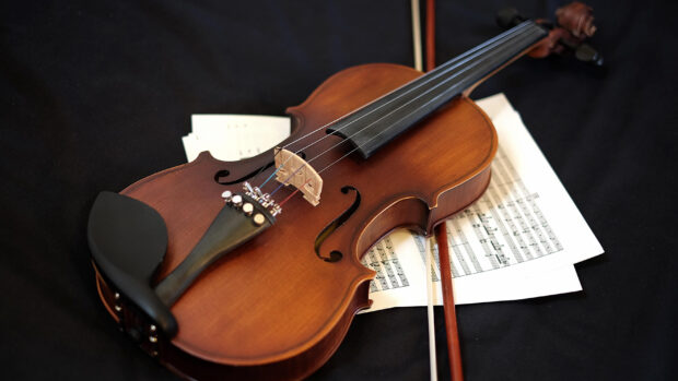 A classic violin lies on musical sheets with its bow on a dark surface, 2K Desktop Wallpaper