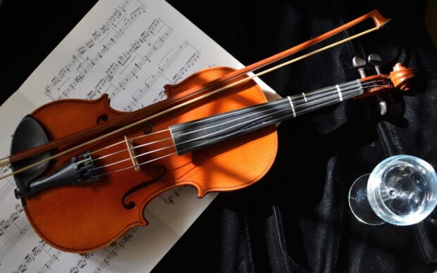 A classic violin with a bow rests on sheet music and a black velvet surface next to a glass of water, HD Desktop Wallpaper