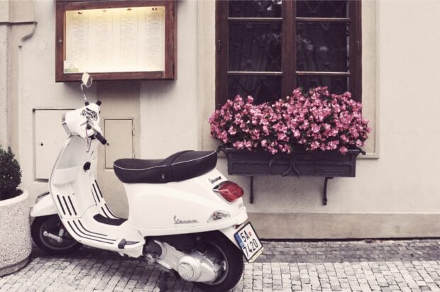 A classic white scooter parked on a cobblestone street next to a window adorned with pink flowers, HD Desktop Wallpaper