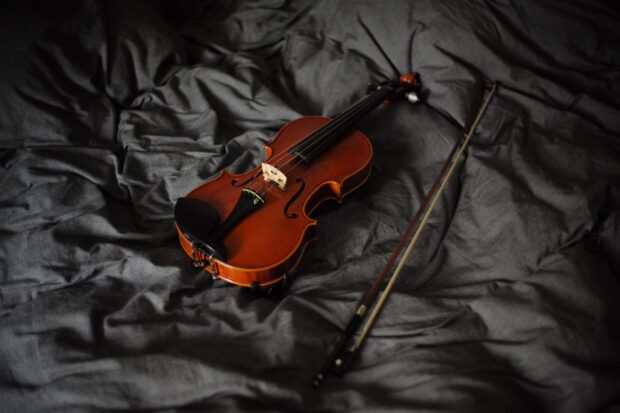 A classic wooden violin with bow resting on dark textured fabric in a close up view, 2K Desktop Wallpaper