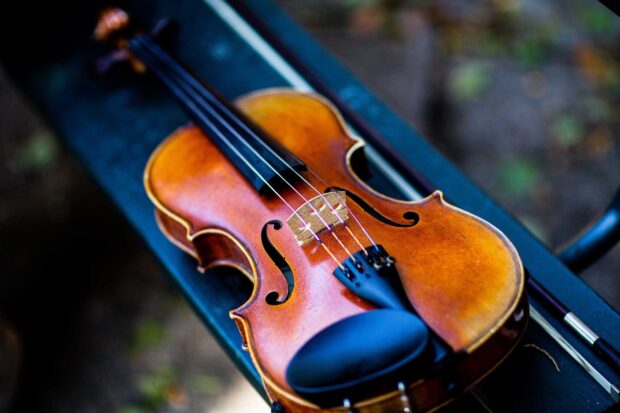 A classic wooden violin resting on a bench with detailed strings and bridge visible, HD Desktop Wallpaper
