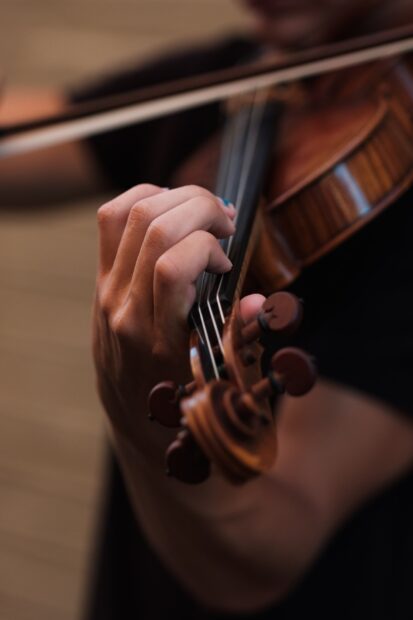 A hand carefully playing the strings of a violin with focus on the instrument's details, HD Phone Wallpaper