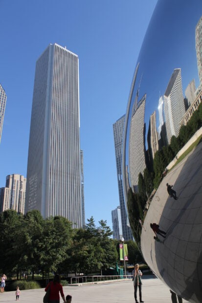 The Cloud Gate sculpture in Chicago reflects nearby buildings and visitors on a clear day, 2K Desktop Wallpaper