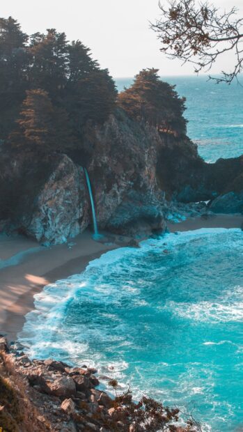 A coastal cliff with a waterfall flows into the ocean under scenic blue skies for scenery wallpapers, HD Mobile Wallpaper