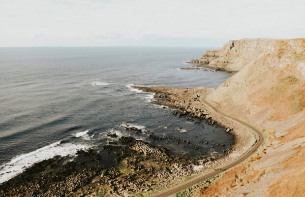 A winding coastal road curves along the rocky shoreline in Northern Ireland wallpapers, 2K Desktop Wallpaper