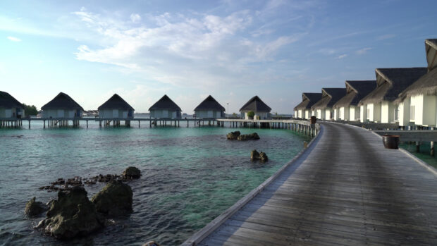 A scenic row of bungalow houses on stilts along the coast with clear blue water, 4K Desktop Wallpaper