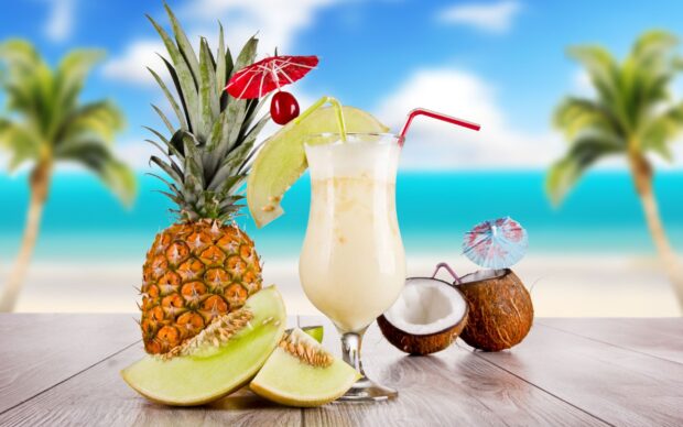 A tropical drink garnished with melon slices pineapple and coconut on a wooden table