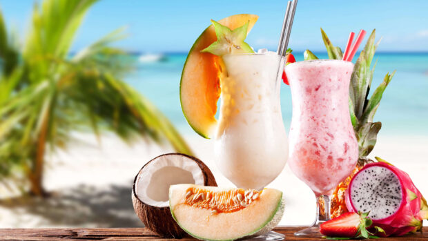 A close up of coconut and tropical fruits with creamy beverages on a beach table