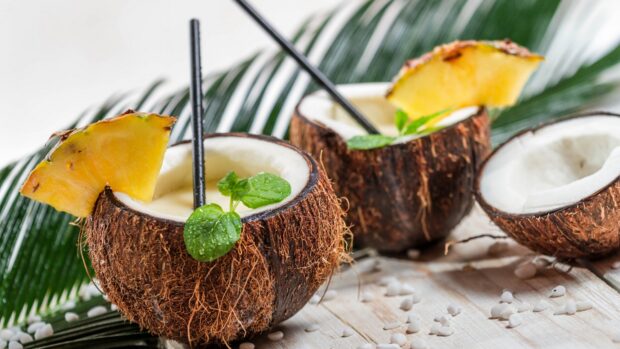Fresh coconut with pineapple slice and mint leaves on wooden table with palm leaves background