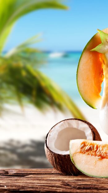 A fresh coconut with melon slices on a wooden table by the tropical beach