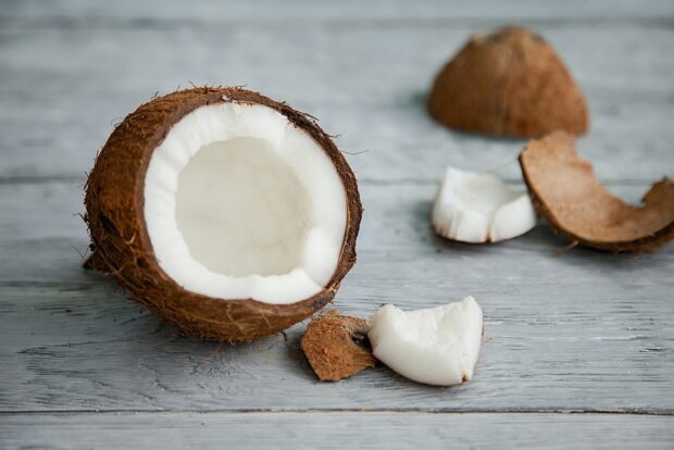 Half coconut with fresh coconut pieces on wooden surface displaying natural coconut texture