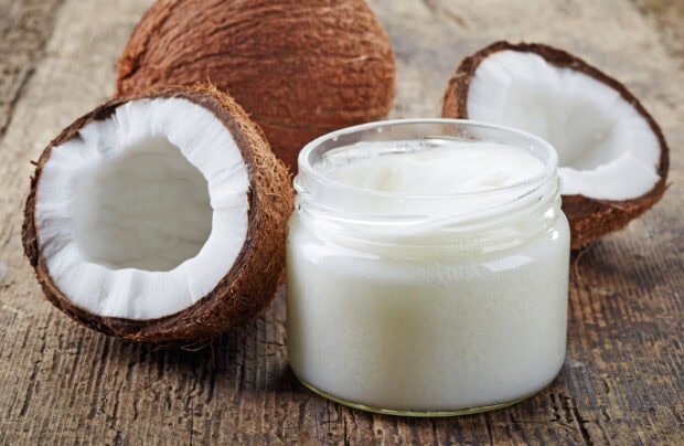 A jar of coconut cream next to cracked coconuts on a wooden surface