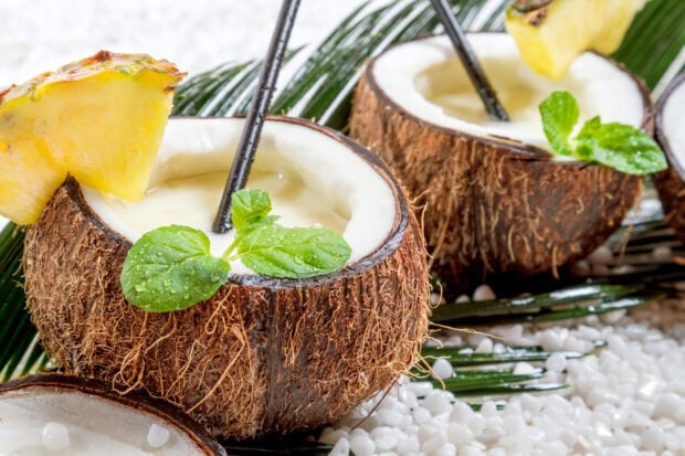 Fresh coconut drink with pineapple slices and mint leaves on white stones