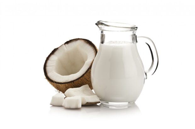 Half coconut with coconut pieces and a jug of coconut milk on a white background