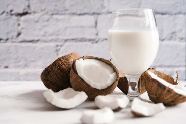 Fresh coconut pieces with a glass of coconut milk on a white surface