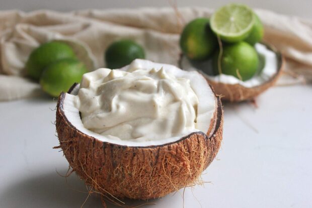Creamy dessert served in a coconut with fresh limes in the background