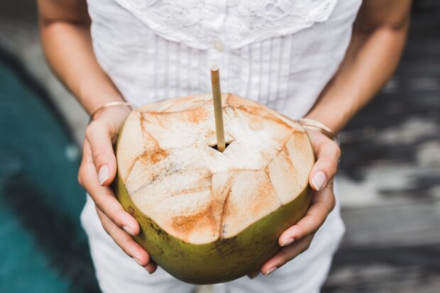 A person holding a fresh coconut with a straw ready to drink