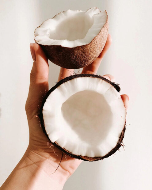 A hand holding two halves of a fresh coconut showing white coconut flesh inside