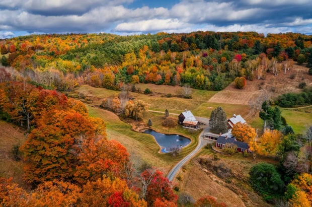 A vibrant Vermont scene with fall foliage surrounding rural houses and a pond, 2K Desktop Wallpaper