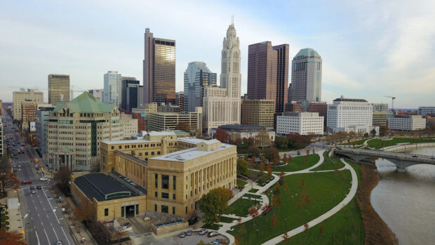 A panoramic view of Columbus Ohio skyline with prominent buildings and green park areas along the river