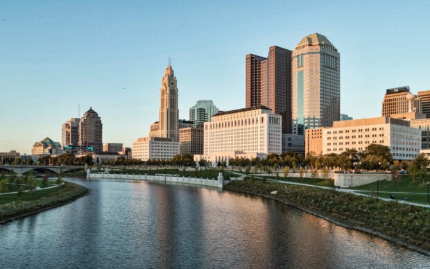 The Columbus Ohio skyline with riverfront greenery and tall buildings under a clear blue sky
