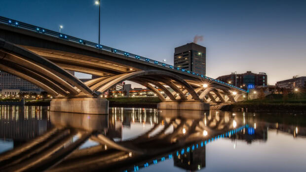 Evening view of the Columbus Ohio cityscape featuring a concrete bridge reflected in the river