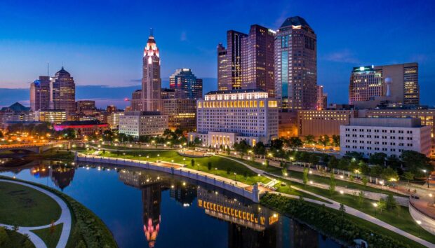 The Columbus skyline at dusk showing city buildings and river reflections in Ohio