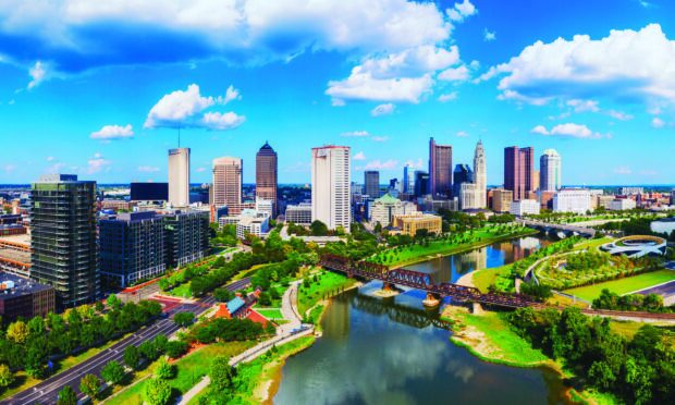 A vibrant skyline of Columbus Ohio with green parks and flowing river under a bright blue sky