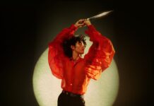 A person in a striking red sheer shirt poses with arms raised against a circular light, HD Mobile Wallpaper