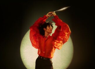 A person in a striking red sheer shirt poses with arms raised against a circular light, HD Mobile Wallpaper