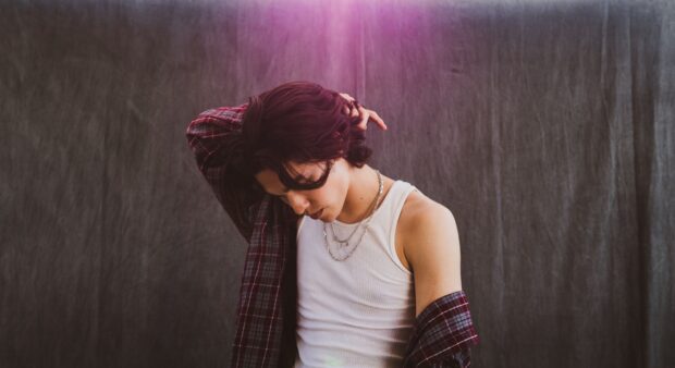 A young man wearing a white tank top and plaid shirt looks downward in a studio setting with a purple light above, HD Desktop Wallpaper