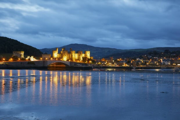 The Wales Wallpapers show Conwy Castle illuminated during dusk with reflections on the water, HD Desktop Wallpaper