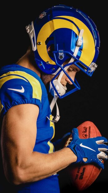 Cooper Kupp wearing a football helmet and gloves holding a football with focus on his arm
