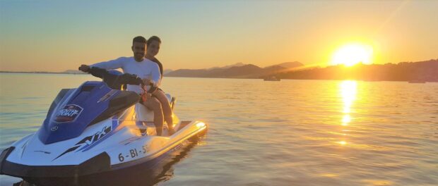 A couple rides a jet ski across calm waters during a beautiful sunset with mountains in the background, 2K Desktop Wallpaper