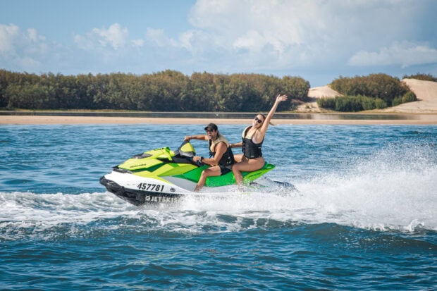 A couple enjoys riding a bright green jet ski across clear water near a sandy shore, 2K Desktop Wallpaper
