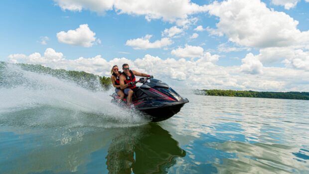 A man and woman in life vests riding a jet ski across calm lake water under a blue sky with clouds, HD Desktop Wallpaper