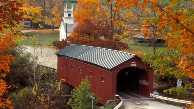 The red covered bridge stands amidst vibrant autumn trees in Vermont, 2K Desktop Wallpaper