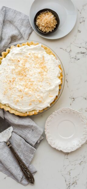 A cream topped pie with toasted coconut flakes ready to serve on a marble surface, 2K Mobile Wallpaper