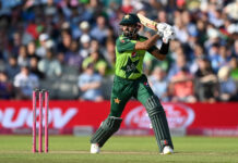 A cricket player in green uniform playing a shot on the field during a match