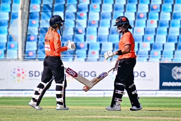 Two cricket players wearing helmets and bats on the field celebrating a partnership