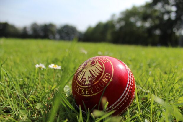 Red cricket ball lying on green grass under clear sky