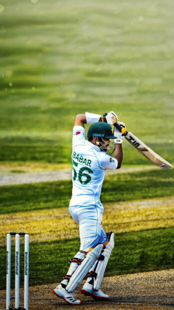A cricket player wearing protective gear is playing a shot with a bat on the field