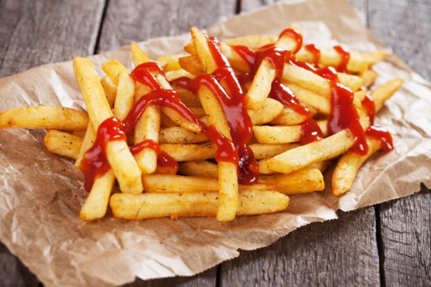 A close up of crispy French fries topped with ketchup on parchment paper, 2K Desktop Wallpaper