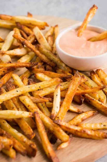 A close up of crispy golden French fries served with a creamy dipping sauce on a wooden board, HD Phone Wallpaper