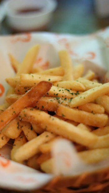 A close up of crispy golden French fries sprinkled with herbs on paper, HD Mobile Wallpaper