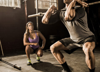 Female fitness trainer coaching man lifting barbell in gym.
