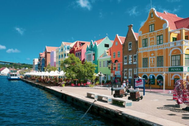 Colorful colonial buildings along waterfront in Curacao with tourists and cannons