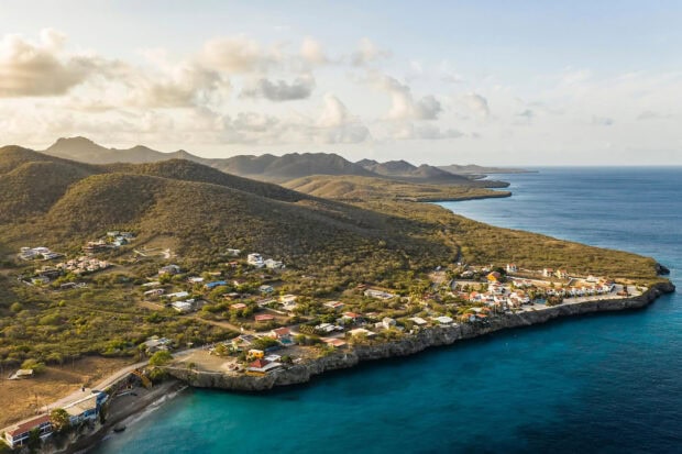 Aerial view of Curacao Island with coastal houses and hills under a partly cloudy sky