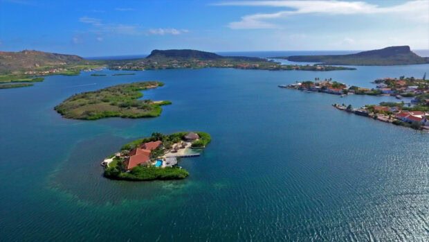 Aerial view of Curacao Island with lush greenery and tropical houses surrounded by blue sea water